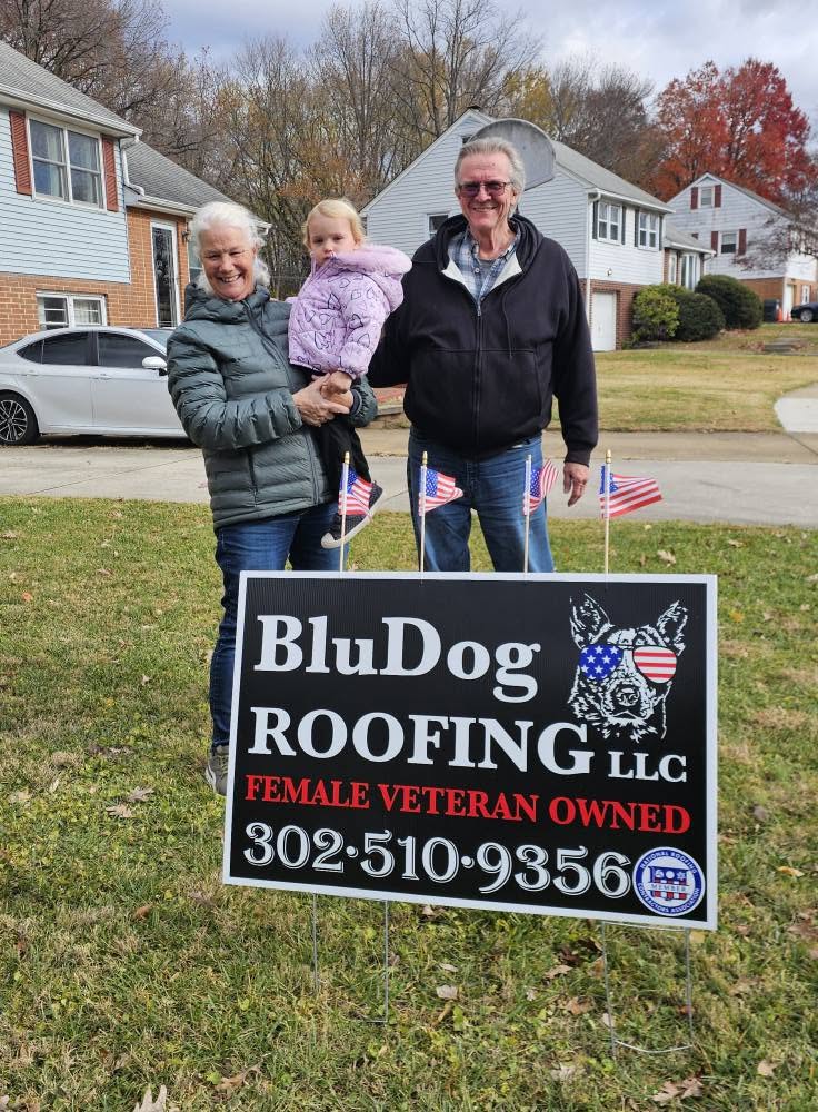 Happy homeowners in front of a BluDog Roofing yard sign